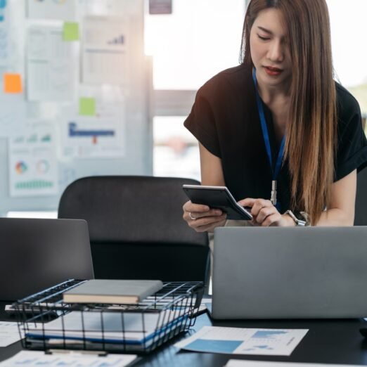 Female businessman working on desk office with using a calculator to calculate cost business report talk smart phone on office desk, finance accounting concept.