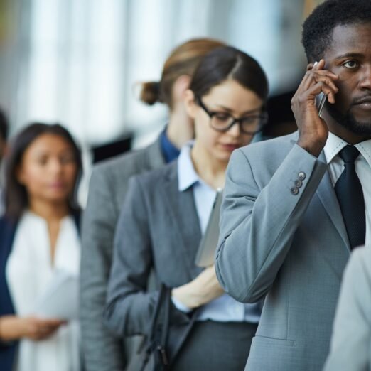 Serious displeased young African-American businessman with beard standing in line and calling on mobile phone while waiting for business forum registration